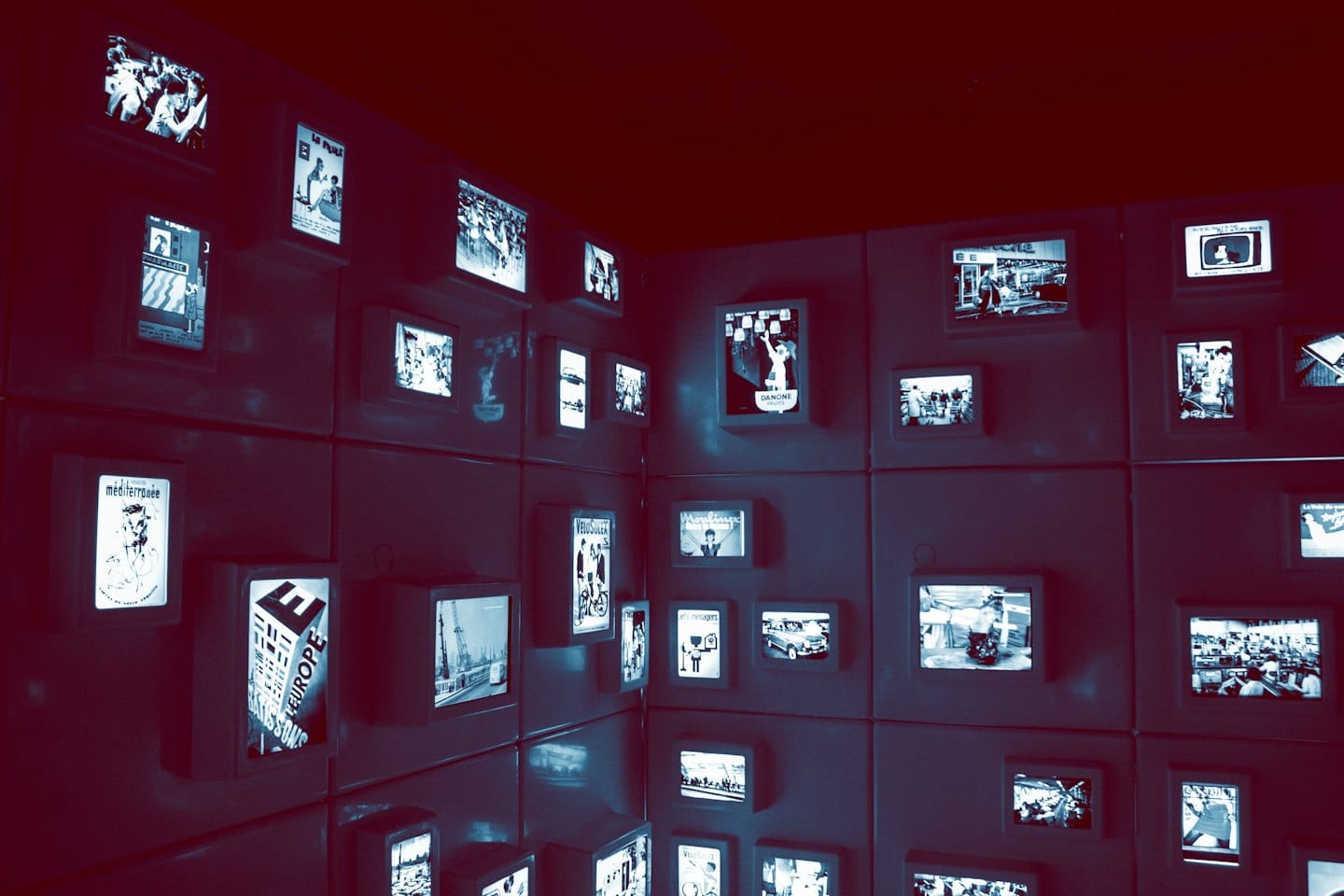 Illuminated screens displaying historical images line a dark museum wall.