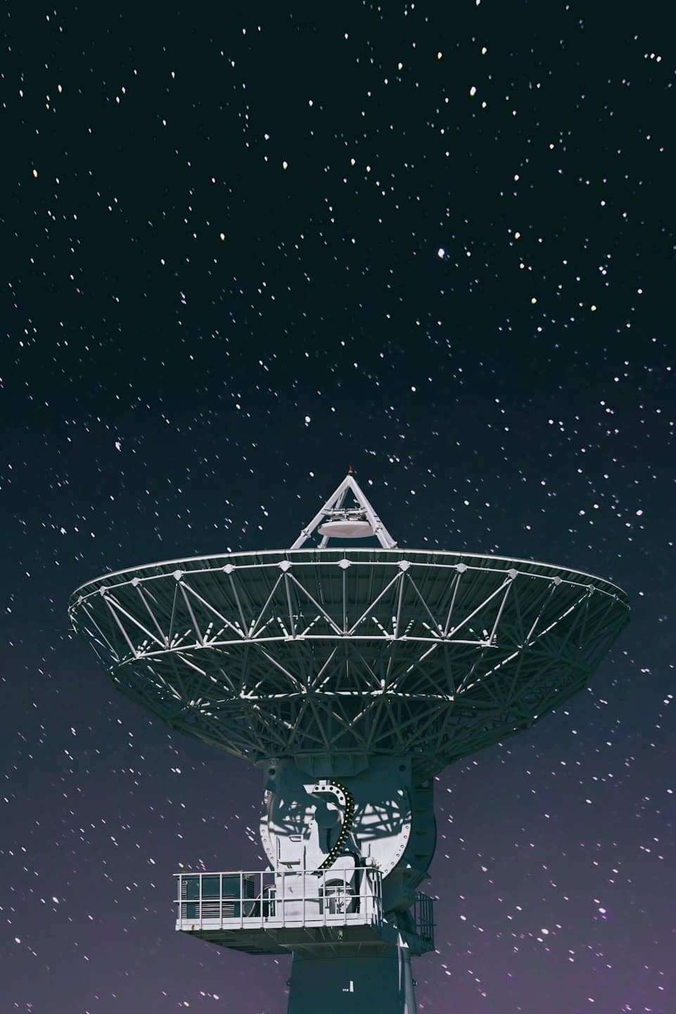 Large metallic satellite dish points towards a starry night sky.
